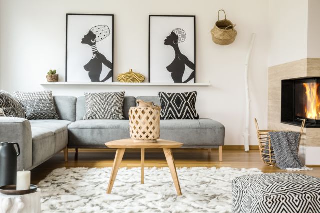 Wooden table on carpet in african living room interior with patterned cushions on grey sofa. Real photo