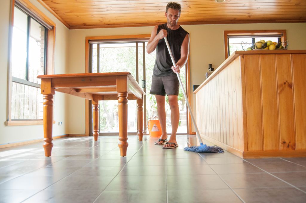 Man cleaning by moping the dining room floor tiles of a middle class family home.