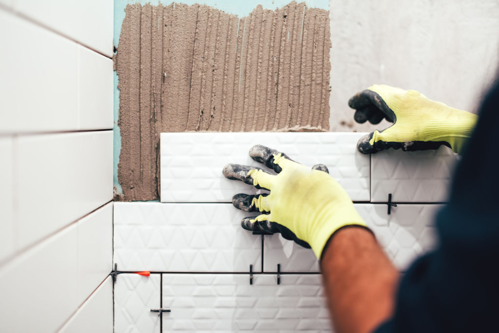 Worker installing small ceramic tiles on bathroom walls and applying mortar with trowel