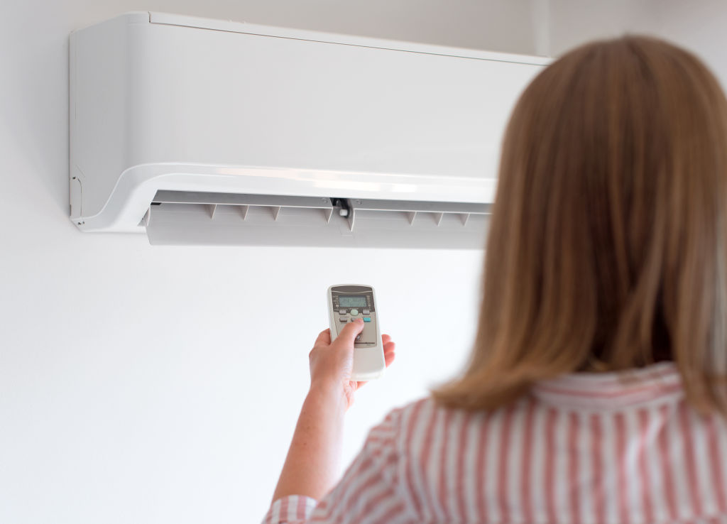 Woman holding remote control aimed at the air conditioner.