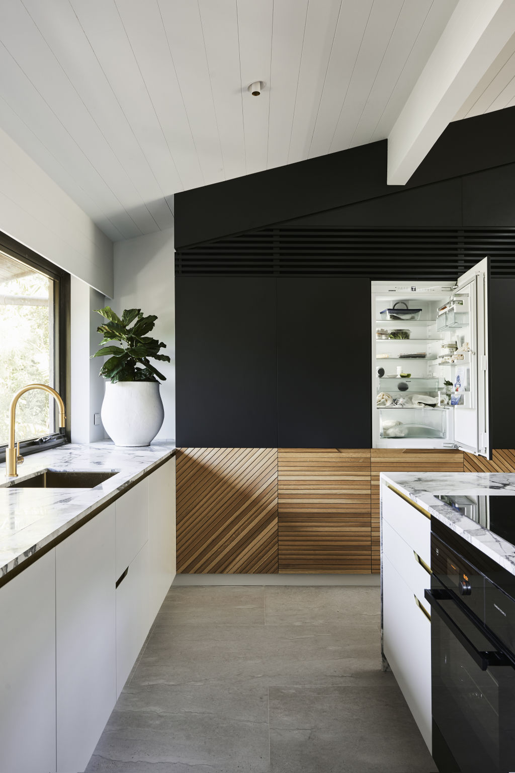 The kitchen, with brass features and a hidden fridge/freezer. The couple had to ‘get creative’ with installing an air conditioner, opting to make a design feature out of it by installing a grill above the kitchen cupboards, which broke up the tall charcoal cabinetry. Photo: Nikole Ramsay