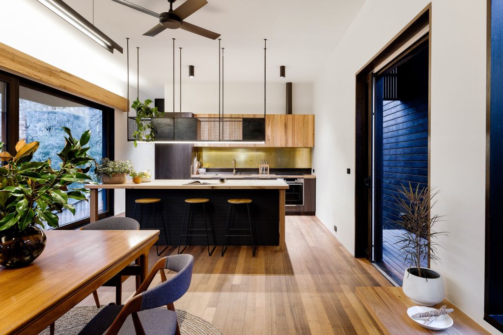 The warm glow of the kitchen with black detailing that features a recycled messmate bench. Photo: Jellis Craig