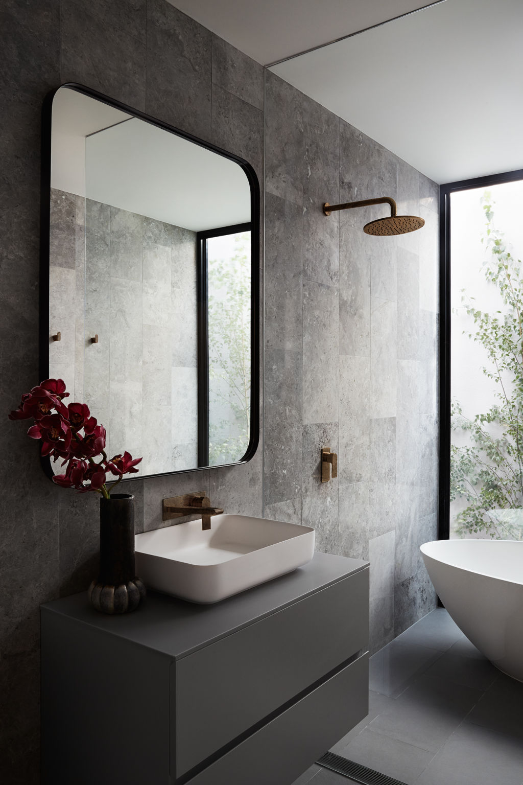 Brass tapware, grey tiling and a curved bath and wash basin feature in the elegant bathroom.  Photo: Fi Storey