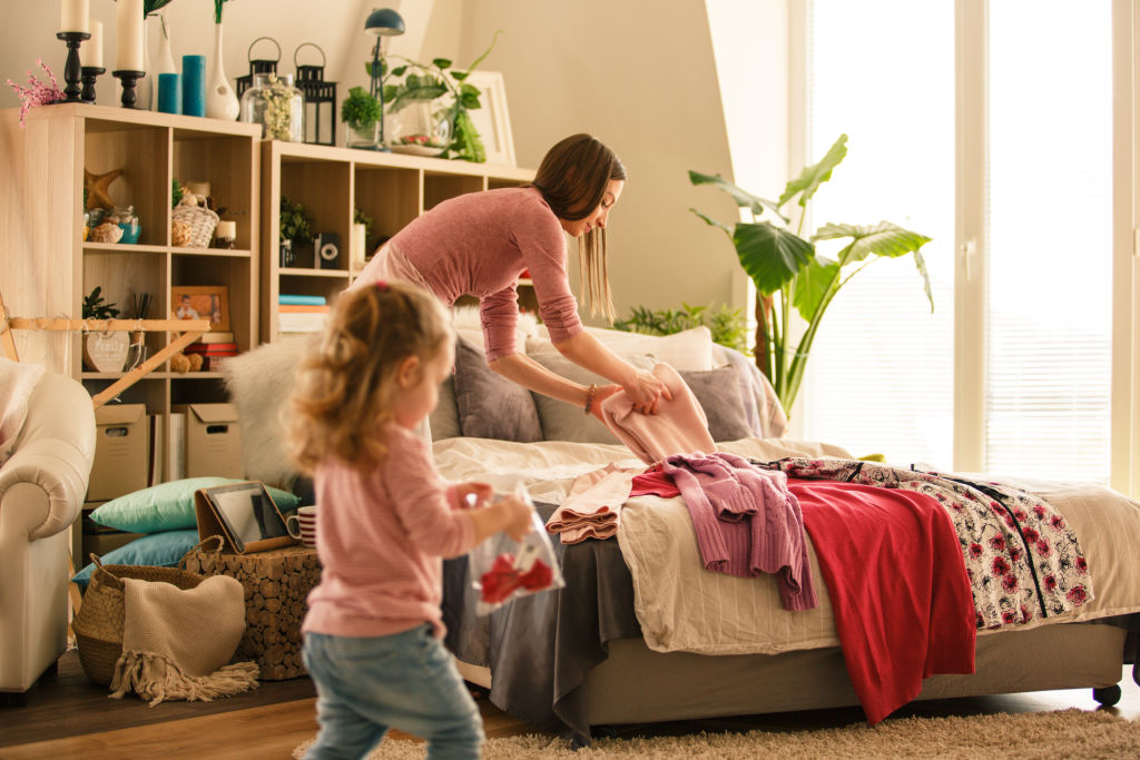 Mother and her little baby girl folding clothes in their bedroom. They are preparing for packing for vacation.