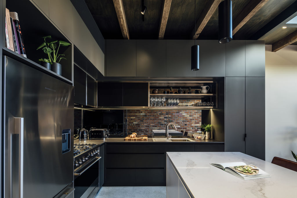 Dark kitchen cabinetry and a dark mirror reflect the recycled brick wall. Photo: Michael Kai
