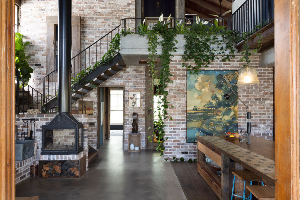 The kitchen and dining zone has exposed brick walls, a slow-combustion fireplace and ceilings soaring to 7.5 metres, inspired by country sheds. Photo: Louise Roche - The Design Villa