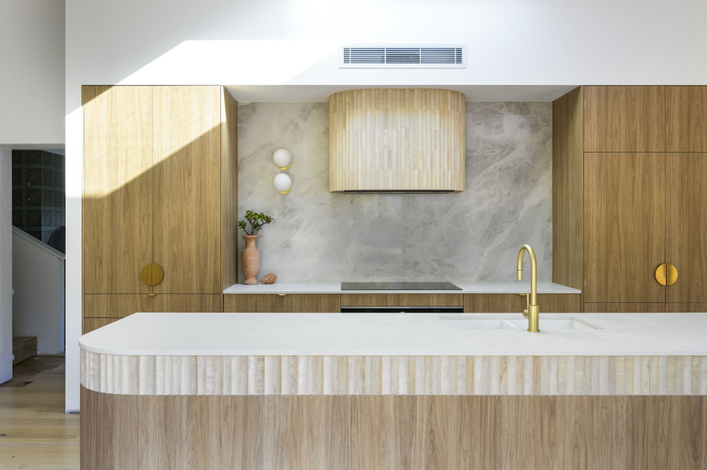 The new kitchen features concave travertine tiles, marbled splashback and wood-toned cabinetry. Photo: Atelier Photography