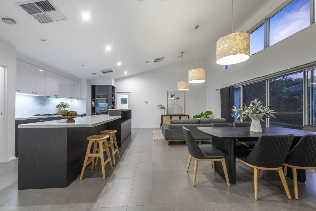 An open-plan kitchen and living area with marbled stone surfaces and dark joinery, raked ceilings, pendant lighting