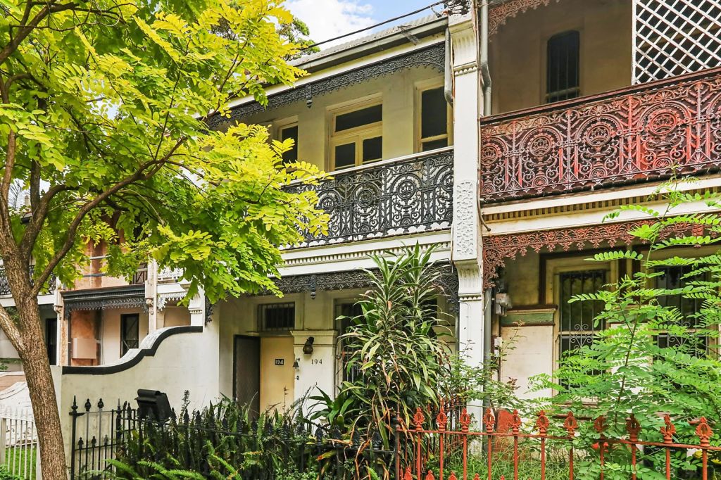Facade fo a double level Victorian terrace with iron work balcony and overgrown garden
