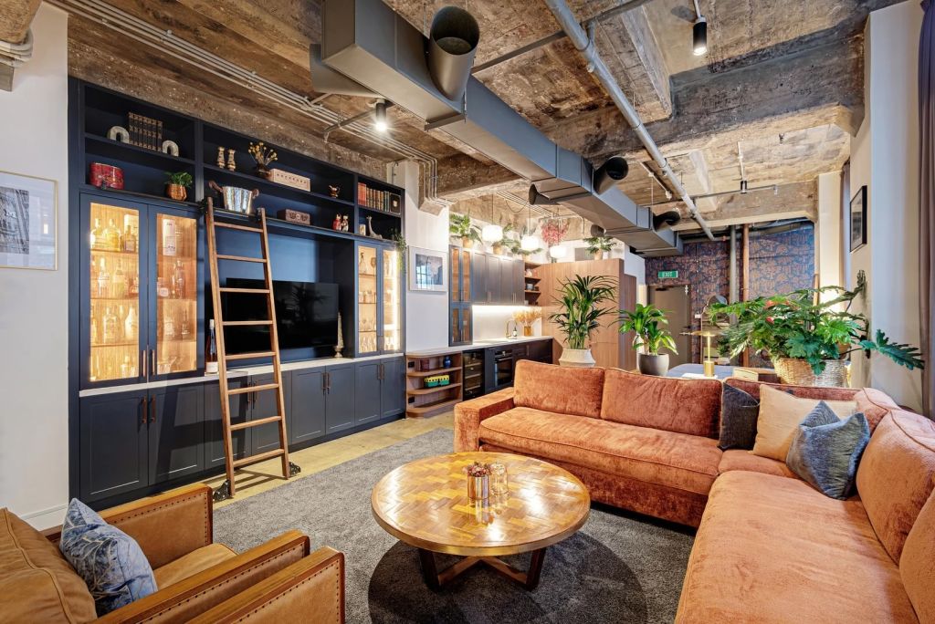 A warehouse converted studio with a living room with orange sofas, polished concrete ceilings and floors and navy blue joinery