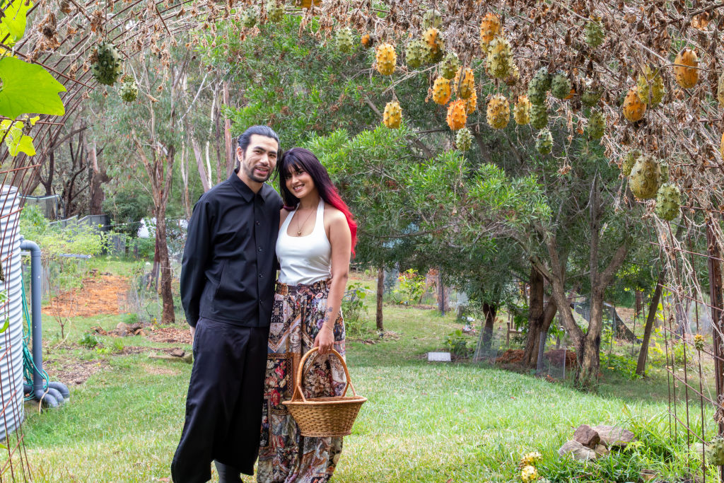 A man and woman stand together in their garden holding a woven basket.